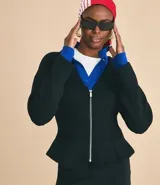Campera femenina de punto roma en color negro, con diseño acinturado y efecto peplum. Presenta cierre frontal con cremallera metálica, escote en V y bolsillos delanteros.