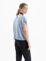 Chaleco de tejido de punto en color celeste, con cuello redondo y mangas cortas con terminación en rib. Presenta un diseño holgado con aberturas laterales en el ruedo y un pequeño bordado decorativo en la parte inferior.