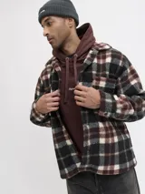 Sobrecamisa de textura tipo teddy con estampado de cuadros en tonos marrón, negro y crema. Presenta cuello camisero, cierre frontal de botones, bolsillos en el pecho y puños abotonados, con un corte relajado.