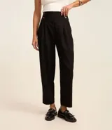 Pantalón zanahoria de sastrería color negro, con cintura alta, pliegues y botones decorativos en los laterales.