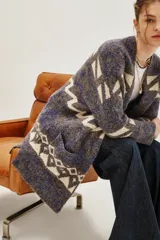 Tapado tipo cárdigan de tejido de punto con diseño geométrico en tonos azul, gris y crudo. Presenta un corte holgado, mangas largas y bolsillos laterales frontales.