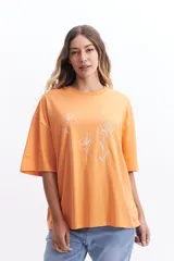 Remera oversize de algodón color naranja con cuello redondo y manga corta. Presenta un estampado lineal de tres flores en color blanco.