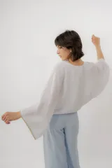 Blusa de lino color blanco, de diseño holgado, manga larga amplia acampanada con detalles de bordado en los puños y cuello redondo.