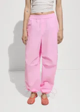 Pantalon estilo parachute de color rosado, con cintura elástica y bajos ajustables mediante cordones. Presenta un diseño holgado con bolsillos laterales.