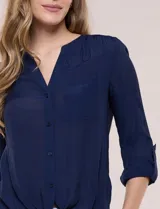 Blusa de calce relajado color salmón, confeccionada en tela liviana con textura sutil. Presenta escote en V con abotonadura frontal, bolsillo parche en el pecho, mangas largas regulables con presilla y ruedo con opción de anudar en el frente.
