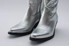 Botas de estilo western (texanas) de caña media, color blanco, confeccionadas en cuero. Presentan bordados decorativos en la caña y puntera cuadrada. Cuentan con cierre lateral y taco de altura media.