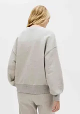 Buzo color crema de algodón, de corte holgado, con cuello redondo y mangas largas. Puños y ruedo acanalados.