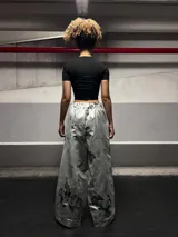 Conjunto de saco y pantalón plateado con estampado de flores negras. El saco es de corte deportivo con cierre y volados en el cuello y mangas. El pantalón es de corte ancho.