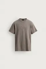 Remera de punto de algodón color gris topo, con efecto lavado, cuello redondo y manga corta. Cuenta con aplicación de parches con texto desgastado en el frente.