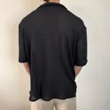 Camisa de manga corta con textura calada y tejido abierto, color negro, con cuello solapa y cierre frontal de botones.