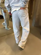 Pantalón deportivo de corte baggy y ajuste oversize, confeccionado en tejido de algodón gris melange. Presenta rayas laterales dobles en color blanco y bolsillos laterales.