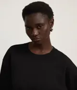 Suéter negro de punto leve, corte boxy, cuello redondo y mangas largas con puños y bajo acanalados.