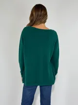 Sweater de punto color verde oscuro, con cuello redondo, manga larga y diseño holgado. Presenta un detalle decorativo de apliques circulares bordados en el ruedo.
