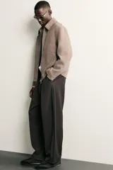 Pantalón de corte balloon fit en color gris oscuro, confeccionado en tejido con viscosa. Presenta pliegues frontales, cintura ajustable con cinturón integrado, bolsillos laterales y bolsillos traseros de doble vivo. Cierre frontal con cremallera y botón.
