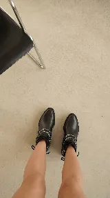 Bota corta de cuero negro con taco cuadrado bajo. Presenta un diseño versátil con un accesorio desmontable que incluye flecos de cuero, tachas metálicas y una cadena decorativa alrededor del tobillo.