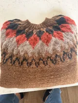 Sweater tejido a mano con diseño de canesú estampado en tonos tierra, negro y naranja. Presenta cuello redondo y una textura suave y abrigada.