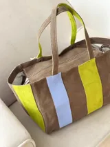 Bolso tipo shopper de diseño amplio, confeccionado en gamuza con un patrón de franjas verticales en tonos marrón oscuro, rosa y verde oliva. Cuenta con doble asa de hombro y cierre superior.
