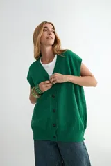 Chaleco de punto color verde, con escote en V y cierre frontal de botones negros. Presenta un diseño holgado con terminaciones acanaladas en el cuello, sisas y ruedo.