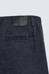 Bermuda de corte relajado confeccionada en denim de algodón rígido, con pliegues frontales, bolsillos laterales y bolsillos traseros de vivo. Cuenta con cierre frontal de cremallera y botón.