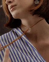 Choker marrón de gamuza con dije de doble aro entrelazado, uno liso y otro con incrustaciones de strass. Los extremos del choker tienen detalles de cuentas doradas.