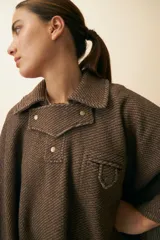 Poncho de lana fina sin teñir en color beige, con cuello camisero, cartera con broches a presión, bolsillo ojal en el pecho y diseño de corte amplio.