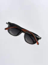 Lentes de sol Osten modelo Maui, con armazón negro de diseño redondeado y detalles en color naranja en las patillas. Cuentan con cristales polarizados con protección UV 400.