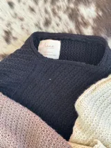 Poncho tejido en lana merino color marrón, con diseño de punto acanalado y terminación con flecos en el borde inferior. Incluye una pequeña etiqueta de cuero en la parte posterior.