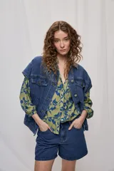 Chaleco oversize de jean negro, con cuello camisero, cierre frontal con botones metálicos y bolsillos delanteros.
