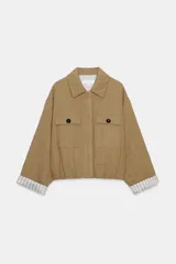 Chaqueta corta de color verde militar, con cuello solapa, bolsillos delanteros con solapa y cierre frontal de botones ocultos. Presenta mangas amplias con vuelta en los puños que muestran un forro a rayas.
