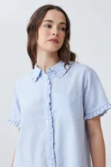 Vestido camisero corto color celeste melange, con cuello camisero y volados en el cuello, la tapeta de botones y los puños de las mangas cortas. Tiene un bolsillo de parche en el pecho.