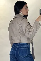 Chaqueta corta tipo biker confeccionada en gamuza color beige, con cierre frontal cruzado, solapas amplias, bolsillos con cierre y cinturón ajustable en la cintura.