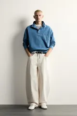 Camisa polo de corte relajado confeccionada en denim ligero de algodón con efecto lavado. Presenta cuello subido, cierre frontal con botonadura oculta por solapa, manga larga, bolsillo de plastrón en el pecho y bajo ajustable con cordón.