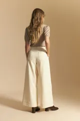 Pantalón largo color crema, tiro alto, de corte recto y ancho. Presenta costuras visibles en contraste y bolsillos delanteros.