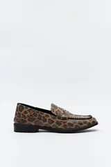 Mocasín de estilo clásico con estampado animal print de leopardo, confeccionado en material texturizado. Presenta detalle de costura decorativa en la capellada y suela plana con pequeño taco.