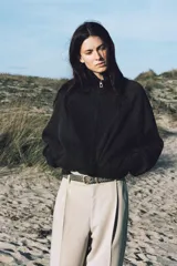 Pantalón negro de tiro alto con pliegues marcados en el delantero y corte ancho en las piernas. Presenta cierre frontal con botón y cremallera, y bolsillos laterales.