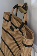 Bolso tipo tote confeccionado en material tejido color tostado con diseño de rayas horizontales negras y asas de mano circulares rígidas envueltas.