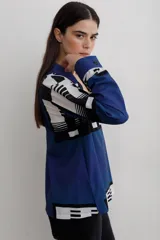 Camisa de manga larga con cuello solapa y cierre frontal de botones. Presenta un diseño estampado con bloques geométricos en tonos azul, blanco y negro.