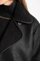 Chaqueta tipo gamulán de color negro con forro de corderito sintético al tono. Presenta solapas anchas, cierre frontal con botones y un diseño entallado al cuerpo.