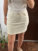 Minifalda de denim color crudo, con diseño de cinco bolsillos, cierre frontal con botón y bragueta, y ruedo desmechado.