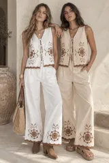 Conjunto de dos piezas compuesto por una musculosa y un short. La musculosa es sin mangas, con escote en V, cierre frontal con tiras para anudar y detalles bordados con diseño floral. El short cuenta con cintura elástica. Las terminaciones de la prenda presentan bordes scalloped (ondulados) con detalles bordados en contraste.