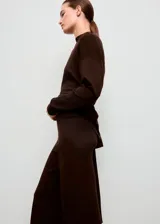Pantalón de punto color marrón oscuro, de tiro medio, cintura con goma elástica y diseño recto y largo. Cuenta con detalle de costuras verticales.