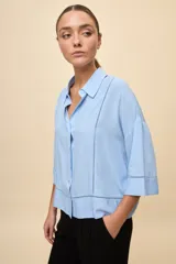 Camisa de calce relajado color celeste, con mangas 3/4, cuello clásico y cierre frontal con botones. Presenta detalles calados en el frente y en las mangas que aportan un acabado delicado al diseño.