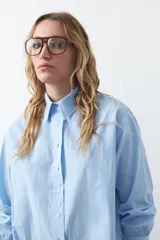 Camisa de corte relajado y diseño clásico, confeccionada en tela de algodón color celeste. Presenta cuello tradicional, cierre frontal con botones y mangas largas con puños rectos.