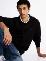 Buzo negro de felpa de algodón con capucha y cordón ajustable, bolsillo tipo canguro, puños y bajo de punto canalé, logo de Tommy Hilfiger bordado en el pecho.