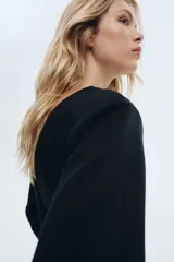 Top de manga larga negro, confeccionado en tejido con textura efecto neopreno. Presenta escote redondo al frente y escote en V pronunciado en la espalda. El calce es entallado en la cintura con un bajo levemente acampanado.