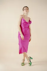 Vestido midi fucsia de satén con escote drapeado, breteles finos y tajo lateral. Presenta una rosa de tela en el bretel izquierdo.