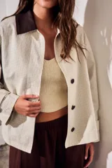 Trench corto de corte oversize con estampado de cuadros finos en tonos beige y verde. Presenta cuello camisero en contraste de color marrón oscuro, cierre frontal con botones y mangas largas con detalle de trabas en los puños.