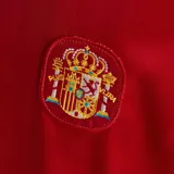 Camiseta de fútbol Adidas retro titular de la selección de España de 1994, de color rojo con cuello polo azul marino y un diseño geométrico de rombos en amarillo y azul marino en el lateral derecho.