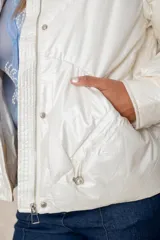 Campera puffer de acabado satinado en color beige, con cuello alto, cierre frontal y bolsillos laterales. Presenta un diseño moderno y sofisticado.