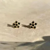 Par de aros dorados con forma de flor y cinco pequeñas piedras negras incrustadas.